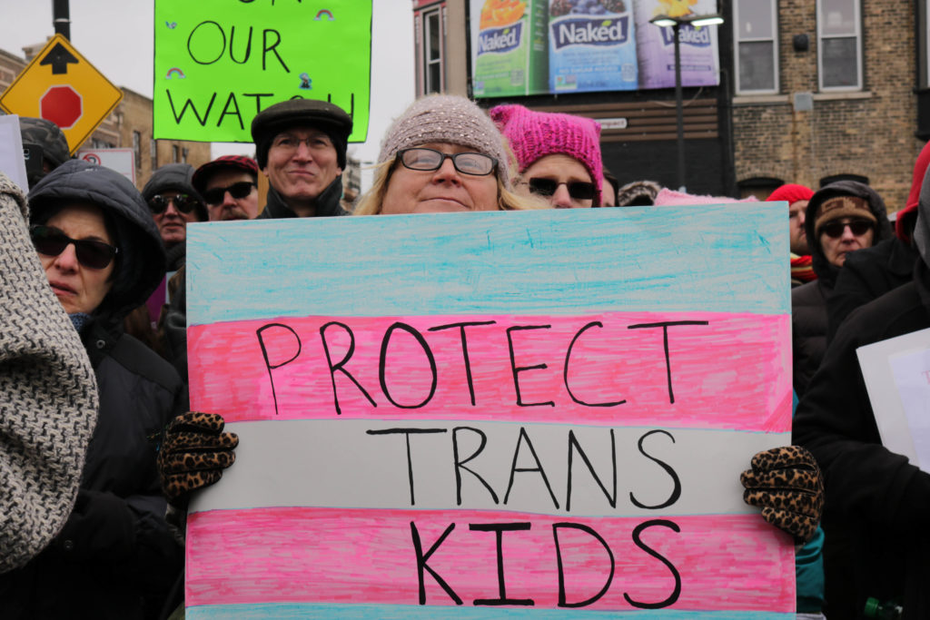A woman holding a sign which says "protect trans kids"