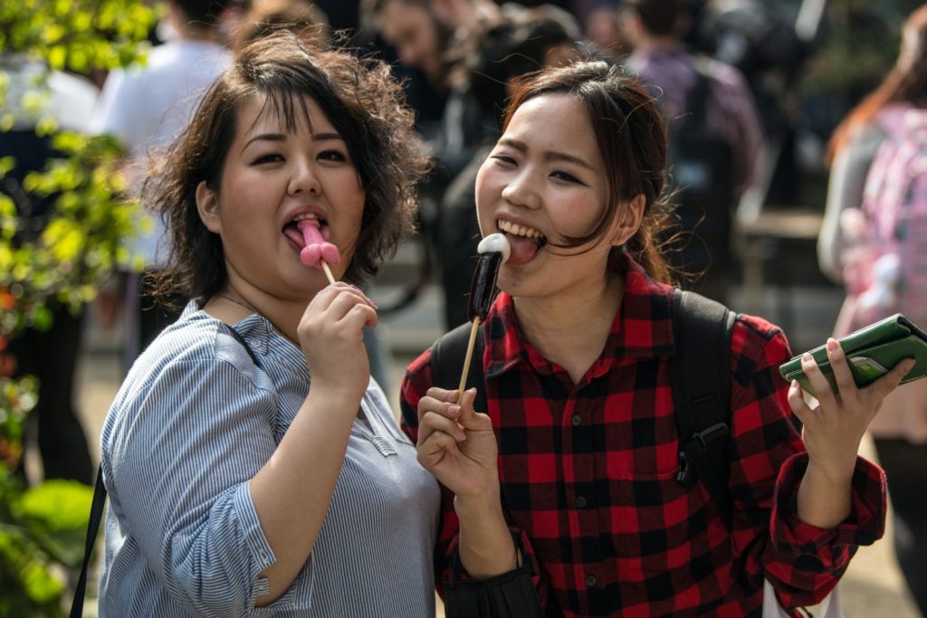 KAWASAKI, JAPAN - APRIL 01: (EDITORS NOTE: Image contains suggestive content.) Women react to the camera as they eat phallic-shaped lollipops during Kanamara Matsuri (Festival of the Steel Phallus) on April 1, 2018 in Kawasaki, Japan. The Kanamara Festival is held annually on the first Sunday of April. The penis is the central theme of the festival, focused at the local penis-venerating shrine which was once frequented by prostitutes who came to pray for business prosperity and protection against sexually transmitted diseases. Today the festival has become a popular tourist attraction and is used to raise money for HIV awareness and research. (Photo by Carl Court/Getty Images)