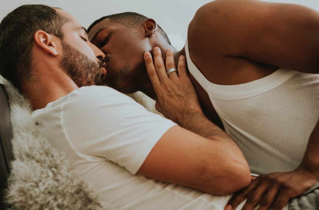Two men kiss on a couch in an example of softcore porn