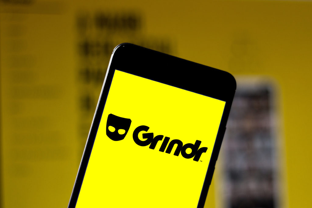 A phone showing a yellow screen with the Grindr logo