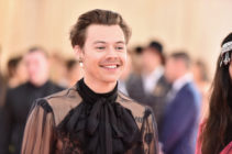 Harry Styles smirks in a lace shirt.