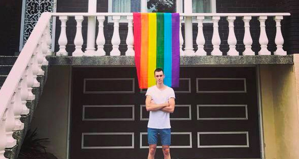 Daniel Comesoli outside of his apartment with a rainbow hanging from his balcony.