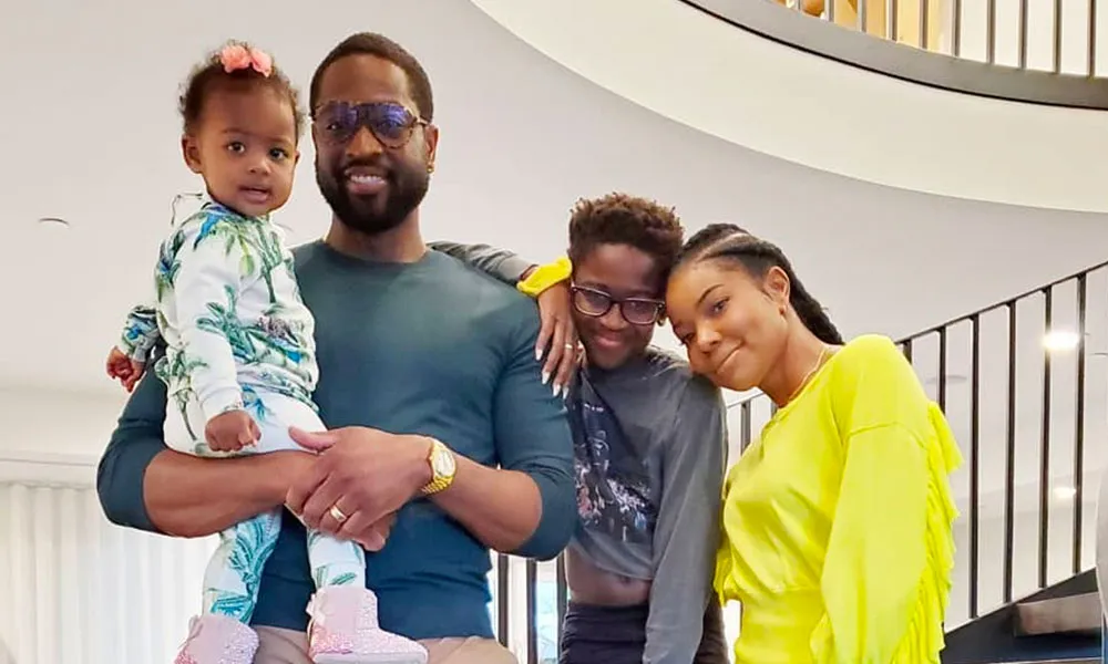 Dwyane Wade holding his daughter Kaavia James, with his child Zion and his wife Gabrielle Union on a grand staircase