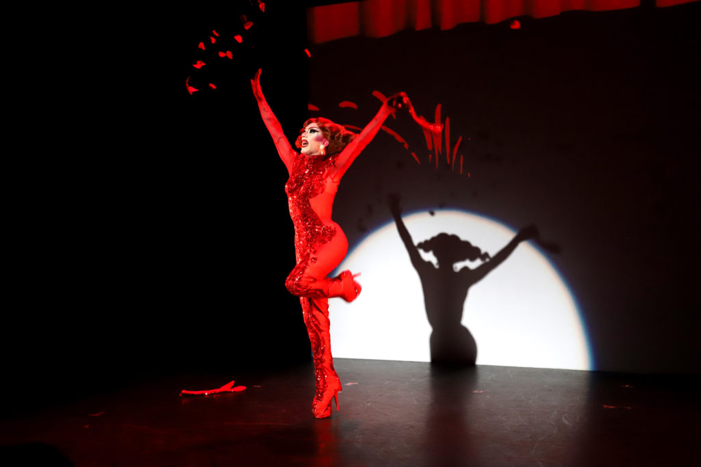 Sasha Velour in a red bodysuit, ripping off a glove to reveal rose petals