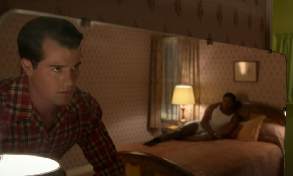 Rock Hudson looking into a mirror as a man lies on a bed in underwear