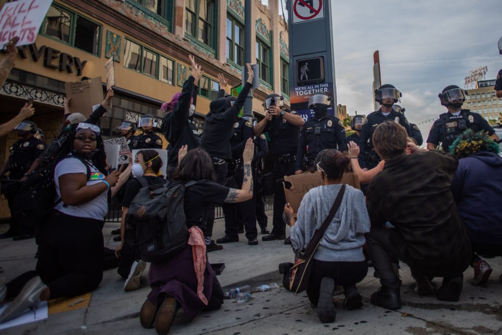 Demonstrators kneel in front of a police line with their hands up while a police officer takes aim towards the crowd in downtown Long Beach on May 31, 2020. (APU GOMES/AFP via Getty Images)