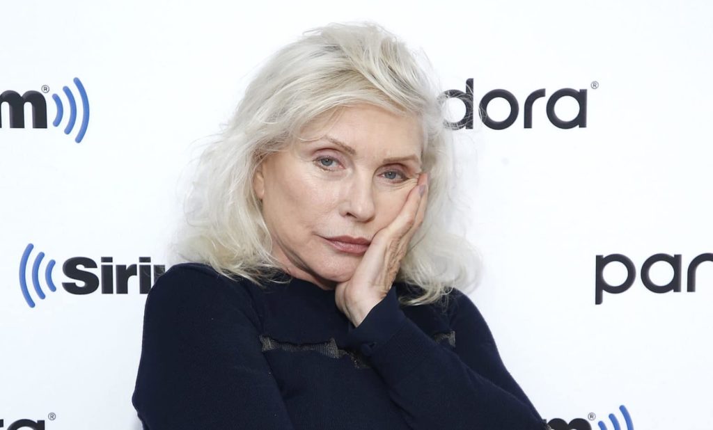 Debbie Harry in a black jumper with silver hair, resting her face on her hand