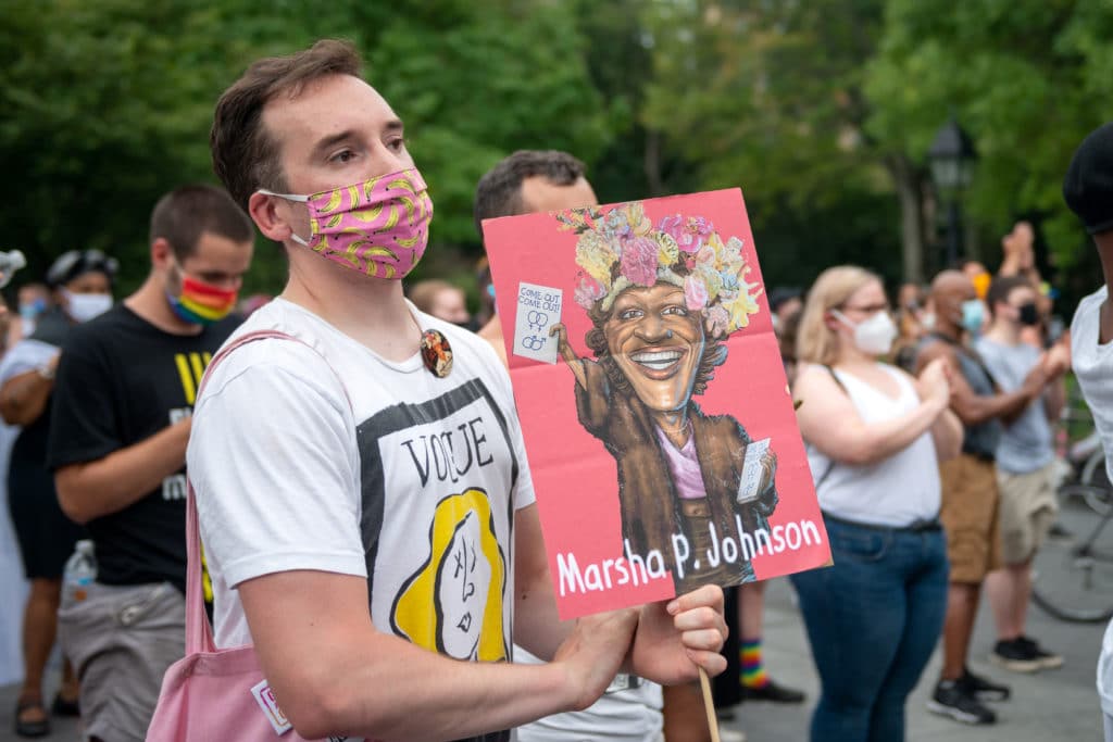 A person wearing a mask holds a "Marsha P. Johnson" sign at the Rally Held On Birthday Of Trans Activist Marsha P. Johnson in Washington Square Park