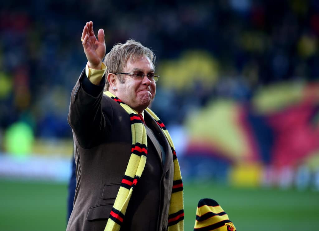 Elton John wearing a Watford FC scarf on a football pitch