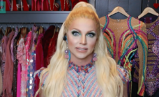 Courtney Act in a drag closet with a rail of glittering dresses behind her