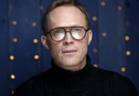 Paul Bettany looking into the camera wearing glasses and a black turtleneck