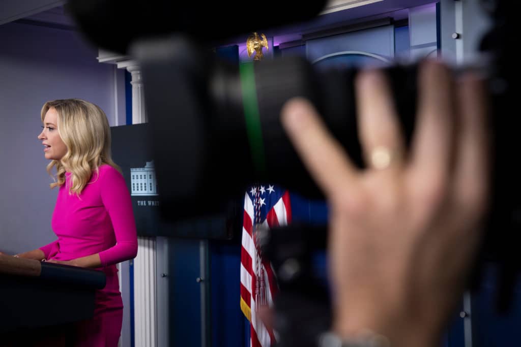 Kayleigh McEnany speaks in a pink dress behind the White House Briefing Room press podium
