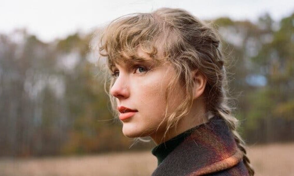 Taylor Swift with her hair in a ponytail, wearing a checked coat, looking off into nature