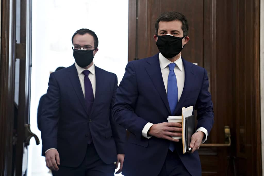 Pete Buttigieg and Chasten Buttigieg, both wearing suits, walk through the doors in the Senate