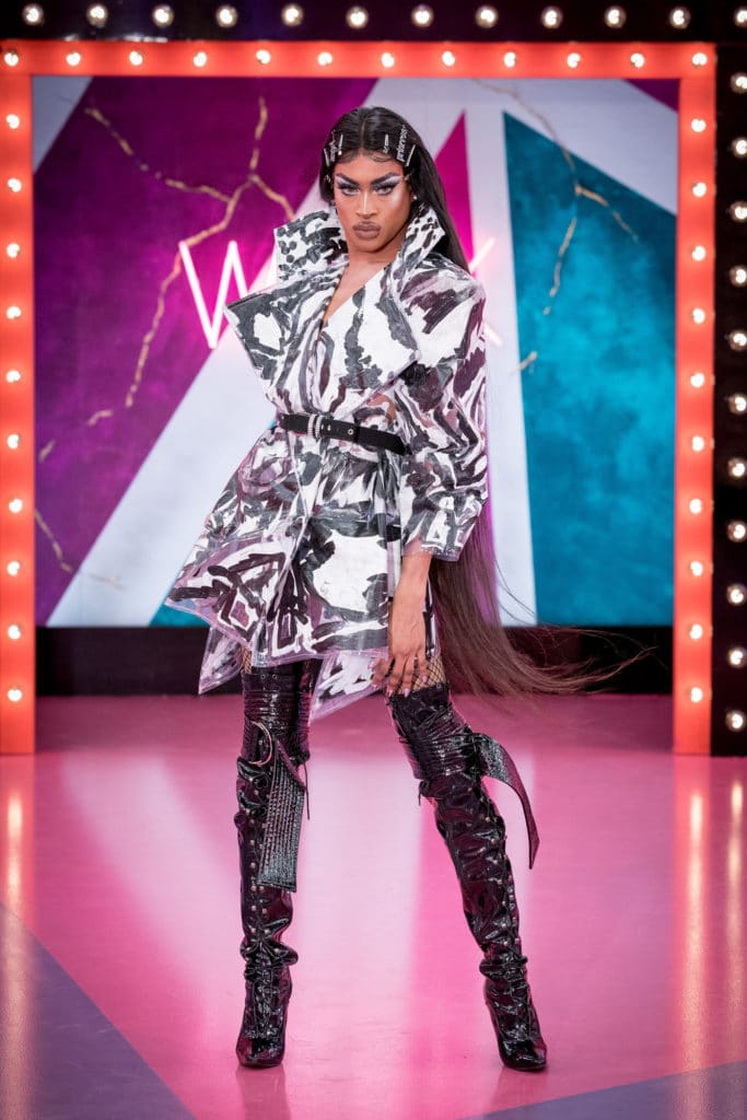 Tayce wearing a laminated black and white coat, waist belt and high black boots