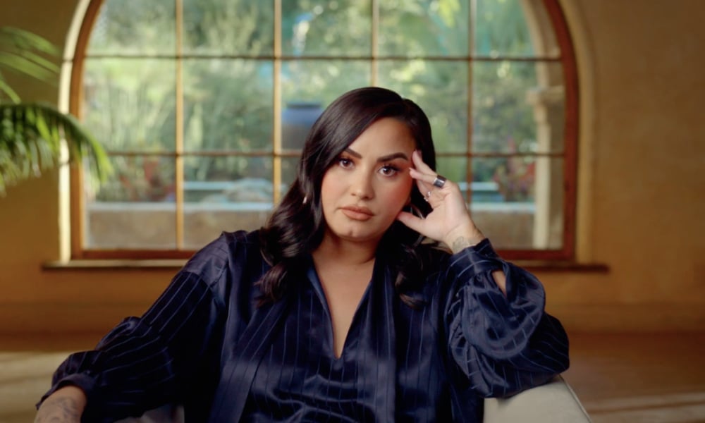 Demi Lovato in the trailer for her documentary, sitting on a chair resting her hand on her face