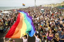 A crowd of pride goers with a giant, long rainbow banner stretching through the crowd
