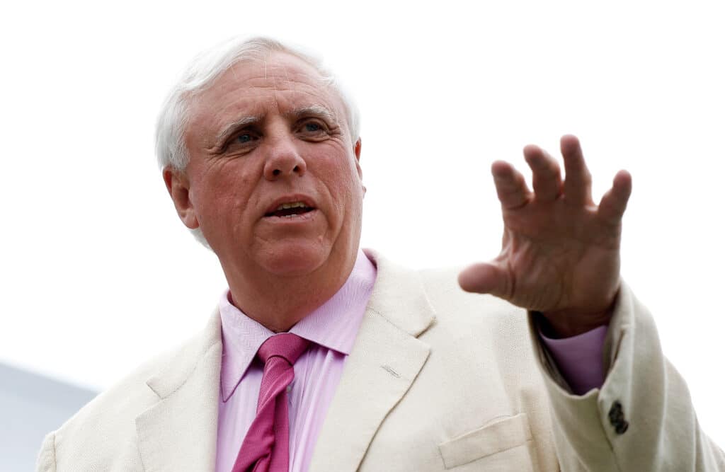 Jim Justice gestures with his hand in a white suit, pink shirt and pink tie outside