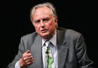 Richard Dawkins gestures while wearing a grey suit and green tie