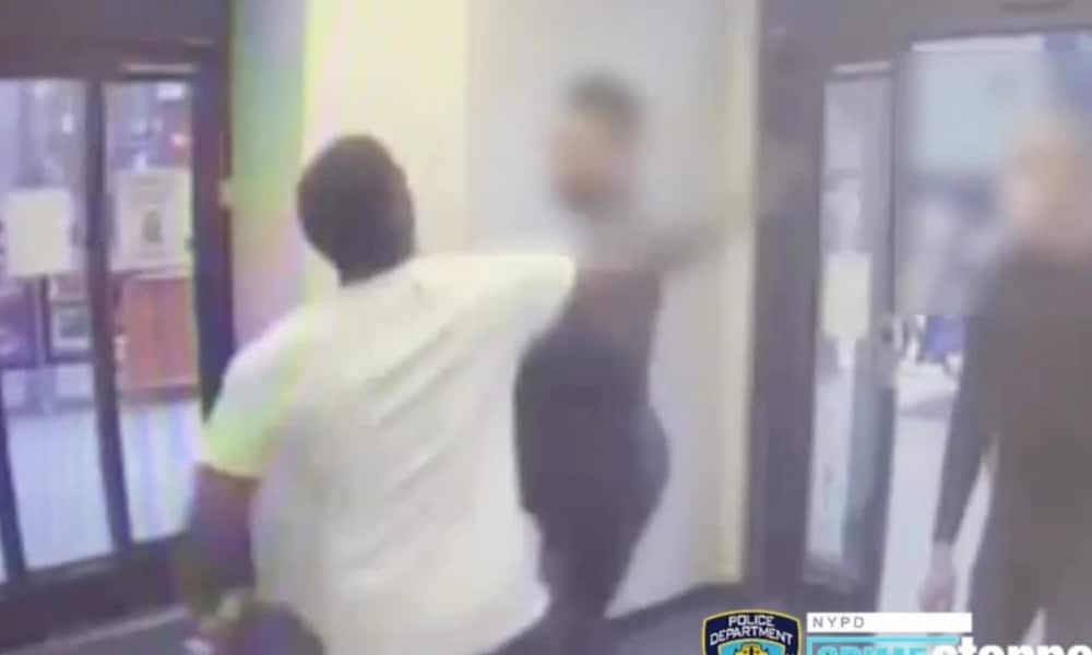 A man in a white tee shirts swings his fist at a man at the entrance of a drugstore