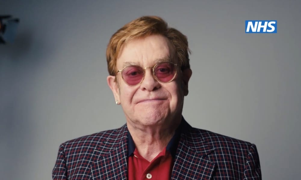 Elton John smiles against a grey background
