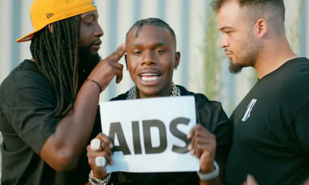 DaBaby holds up a sign with the word "AIDS" on it