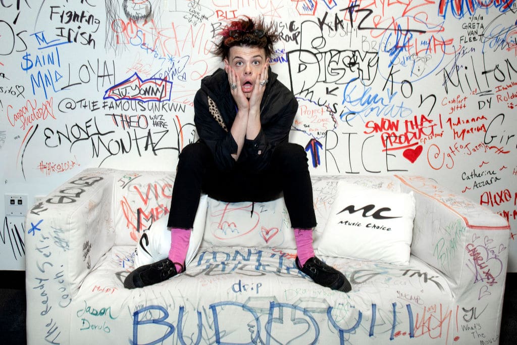 Yungblud, real name Dominic Harrison, visits Music Choice in 2019 and poses against a background of graffiti while sitting on a sofa