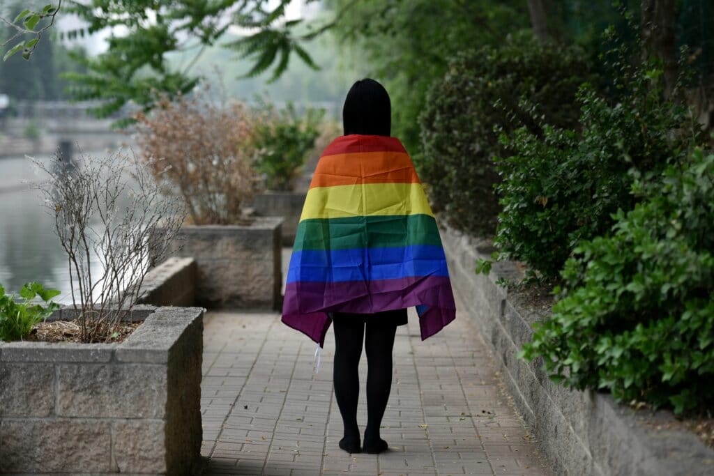 Student with rainbow flag draped over their shoulders, photographer from behind, in Beijing, China