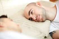 Young man with his head on pillow lying in bed and looking at his lover