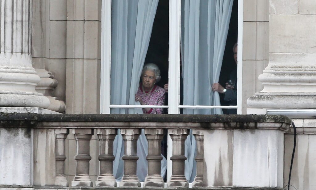 The Queen looking out of her window at Buckingham Palace.