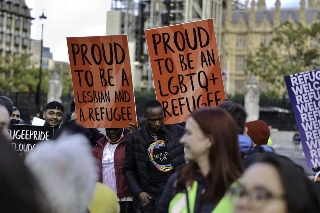 Protesters buttress placards up high standing in solidarity with queer refugees in Parliament Square
