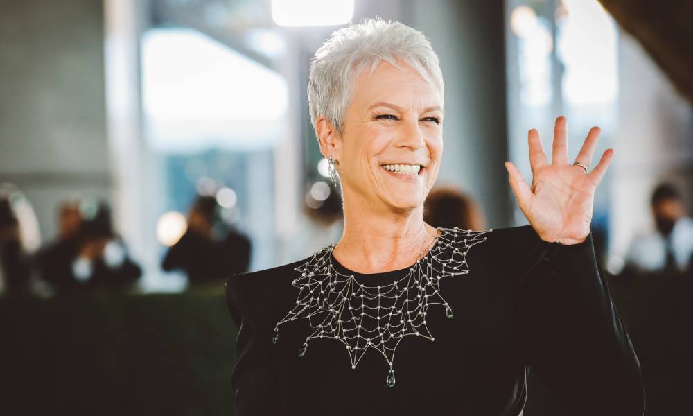 Jamie Lee Curtis waves at the crowds in a black dress with a collar designed to look like spider web