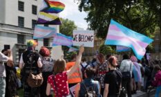 People hold up trans pride flag, non-binary flag and progressive pride flags in a protest outside Downing Street