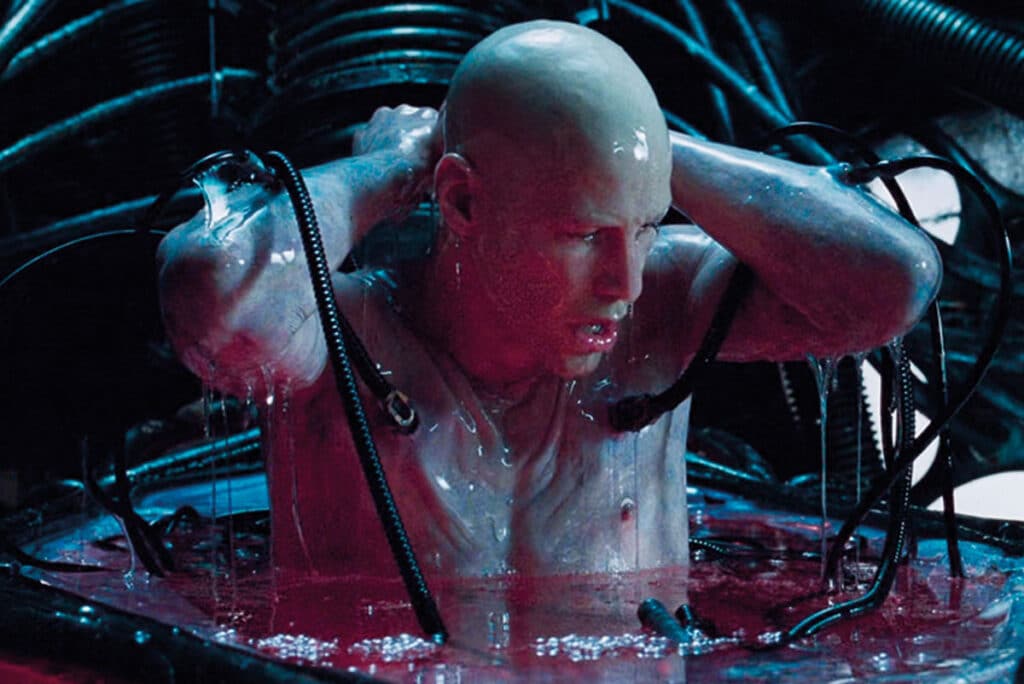Neo, bald and naked, in a pod of liquid with thick wires going into his body