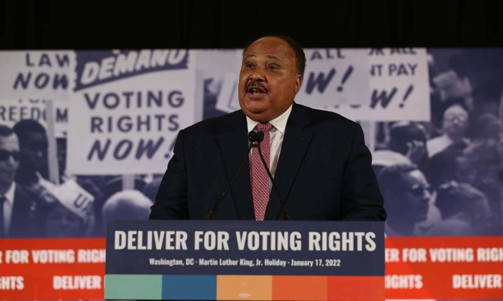 Martin Luther King III stands at a podium with the words "deliver for voting rights" on it