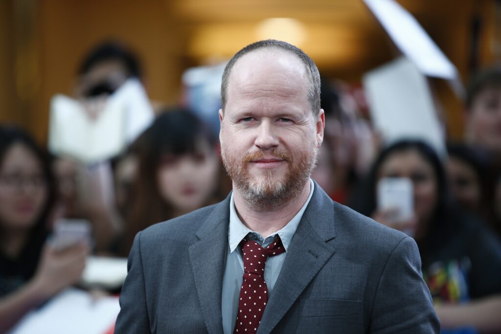 Joss Whedon poses on the red carpet with fans behind him