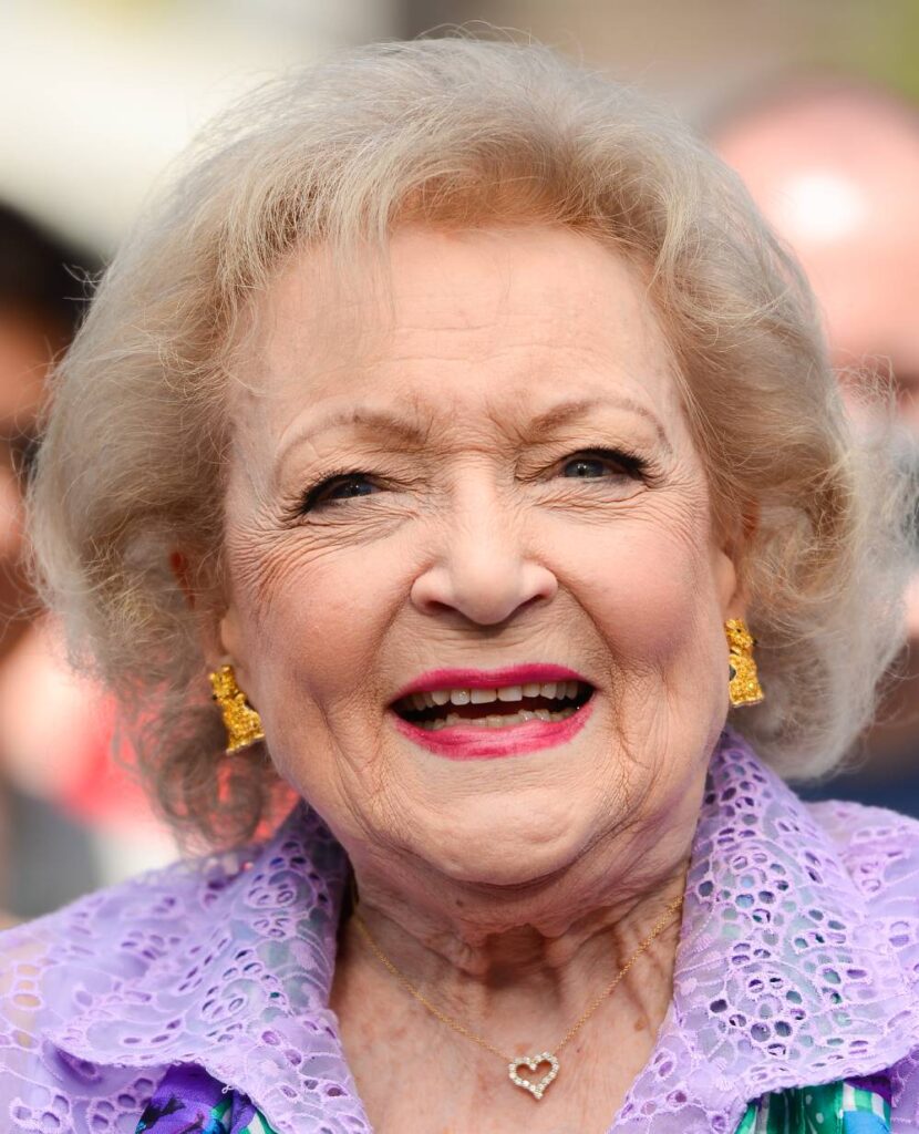 Betty White smiles at the camera while wearing a pastel purple top
