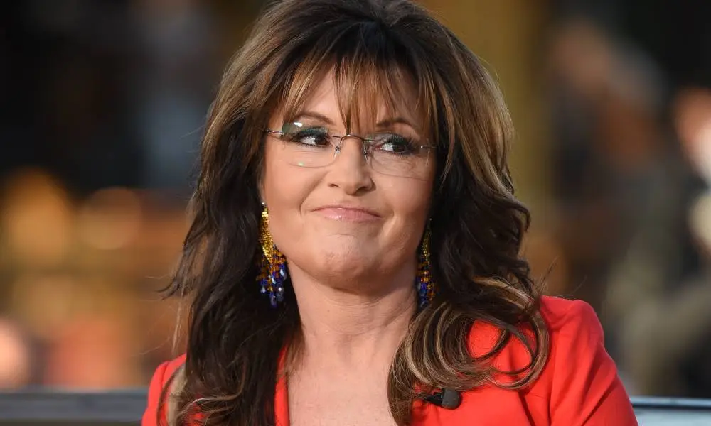 Sarah Palin wears a red coat and glasses on the set of "Extra"