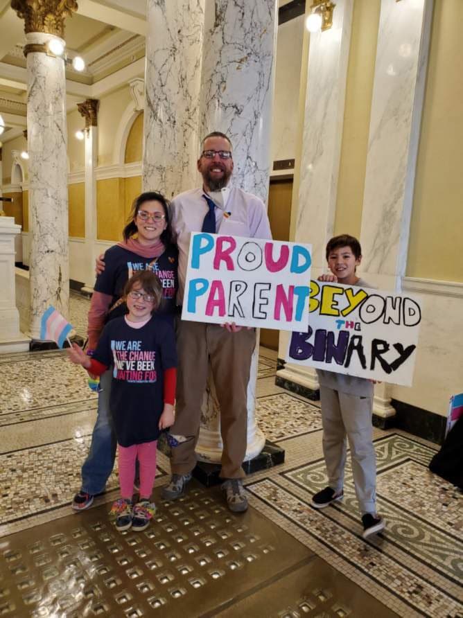 Mike Phelan and his family hold up signs in support of trans and non-binary people in South Dakota
