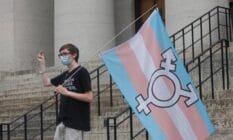 A protester holds the trans flag and snaps in solidarity with other speakers, during a trans rights demonstration
