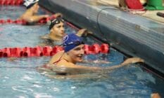 Lia Thomas clutches the side of a pool during a swimming meet and smiles at other competitors