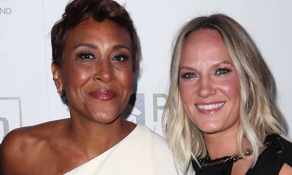 Robin Roberts wears a white dress as she stands next to her partner Amber Laign, who is dressed in a black outfit