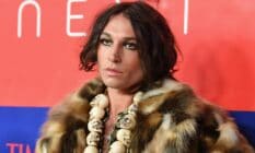 Actor Ezra Miller wears a fluffy brown fur-like jacket with a skull necklace and shiny makeup