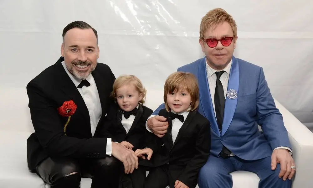 David Furnish and Elton John sit with their sons Elijah and Zachary between them as they pose for a photo while wearing suits
