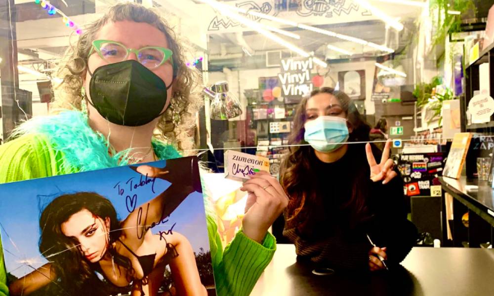 Charli XCX and fan Tabby Lamb pose with signed items including a vinyl copy of Charli's album CRASH and a packet of Lamb's oestrogen