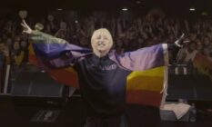Korean singer Holland wears an LGBT+ flag as he performs on stage with a crowd of fans behind him