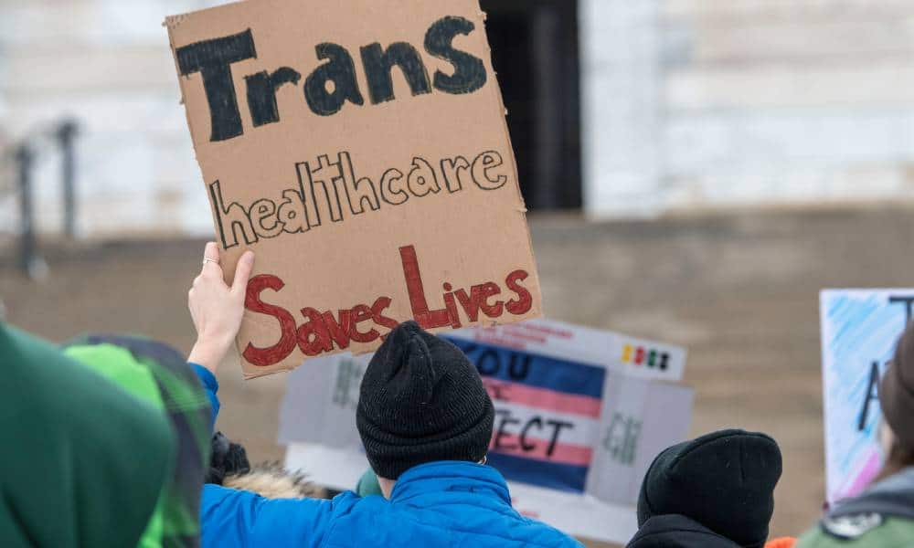 A person holds up a sign that reads "Trans healthcare saves lives" during a protest