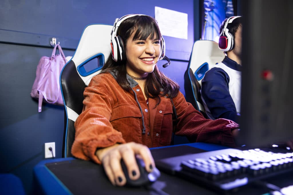 A gamer wearing a headseat, clicking a mouse, smiling