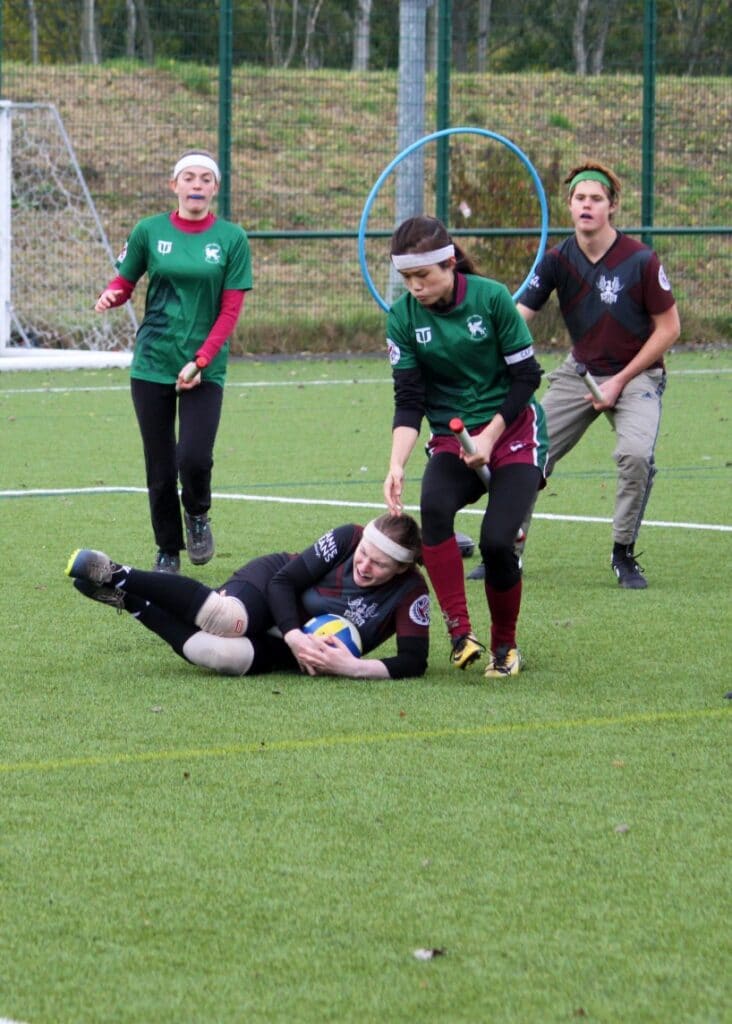 Four quidditch players, one has thrown themself onto the ground catching a ball
