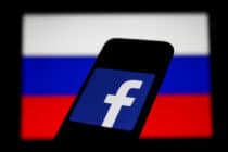 Facebook logo displayed on a phone screen and Russian flag displayed on a screen in the background